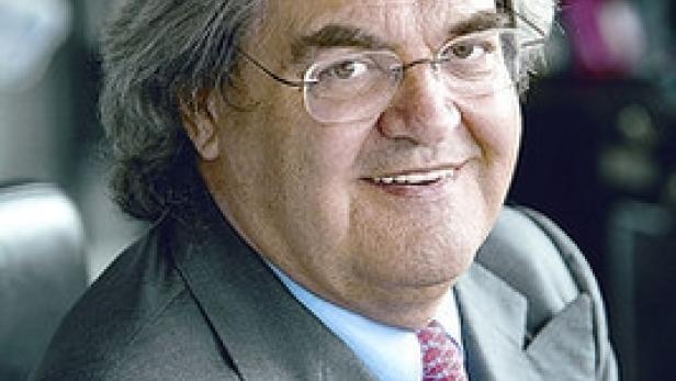 Ein lächelnder Mann mit Brille und grauem Haar trägt einen grauen Anzug.
