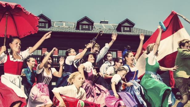 Eine Gruppe Menschen in Tracht feiert mit einer großen Österreich-Flagge vor einem Haus.