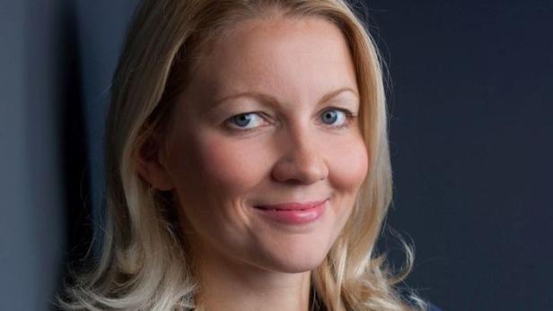 Porträt einer lächelnden Frau mit blonden Haaren vor einem dunklen Hintergrund.