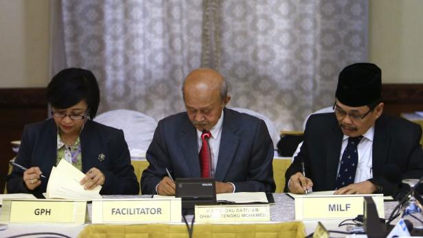 Drei Personen sitzen an einem Tisch und schreiben etwas auf Papier.