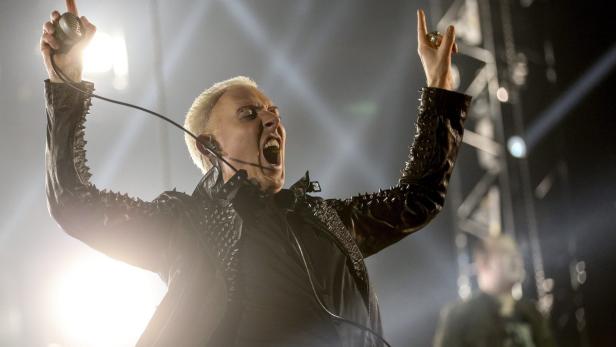 Ein Sänger mit blonden Haaren schreit mit erhobenen Händen ins Mikrofon.