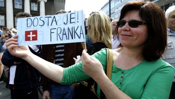 Eine Frau hält ein Schild mit der Aufschrift „Dosta je! + Franka“ und der Schweizer Flagge.