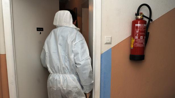 Eine Person im Schutzanzug betritt einen Raum; ein Feuerlöscher hängt an der Wand.