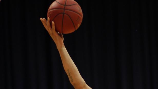 Ein Arm hält einen Basketball vor einem dunklen Hintergrund.