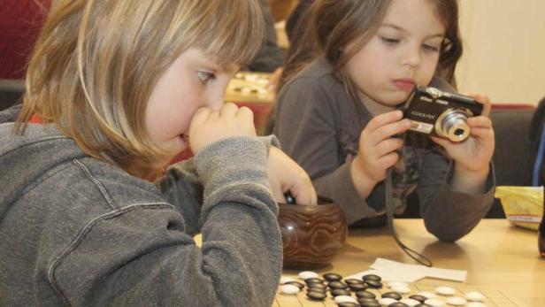 Zwei Kinder spielen Go, eines fotografiert mit einer Digitalkamera.