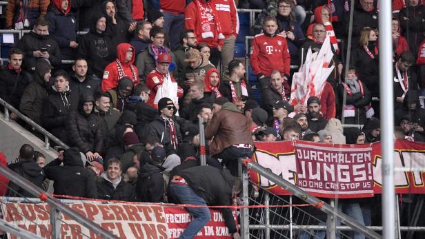 Fußballfans im Stadion, einige klettern über Absperrungen.
