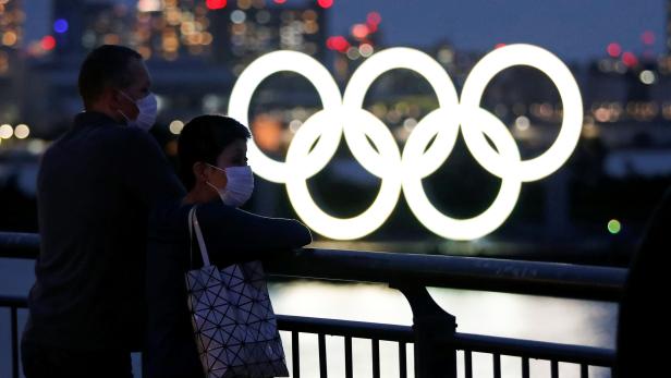 The giant Olympic rings are seen in front of the visitors wearing protective face masks, in Tokyo
