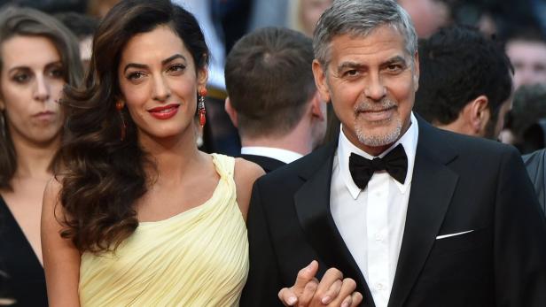 Amal und George Clooney posieren auf einem roten Teppich.