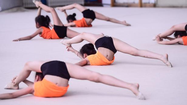 Mehrere junge Turnerinnen dehnen sich auf dem Boden.