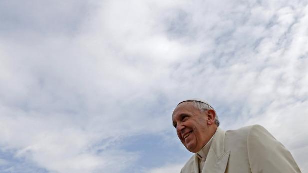 Papst Franziskus lächelt vor einem Himmel mit vielen Wolken.
