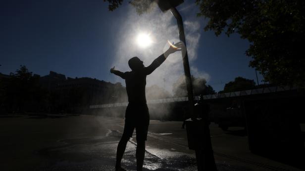 A man cools off under a water sprinkler during a hot summer day in Vienna