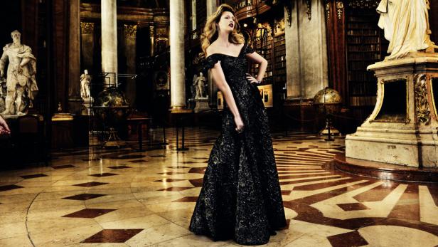 Eine Frau in einem schwarzen Kleid posiert in einer prunkvollen Bibliothek.