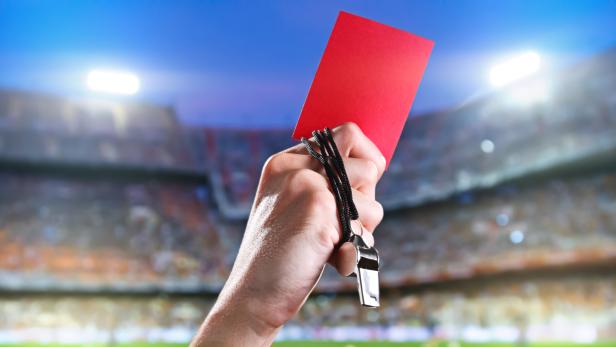 Referee holding up a red card and whistle inside a stadium