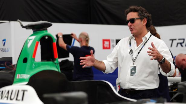 Ein Mann mit Sonnenbrille gestikuliert vor einem grünen Rennwagen.