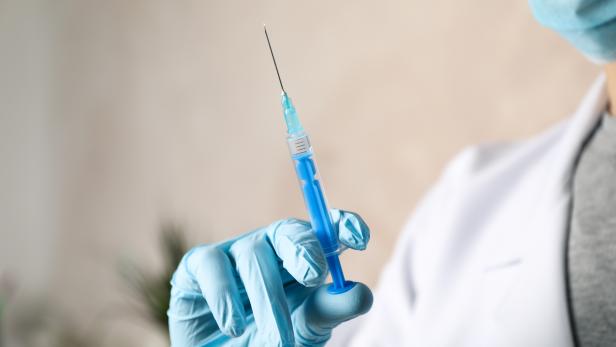 Doctor holds medical syringe of vaccine, injection on brown background. Coronavirus protection. Healthcare and medical concept