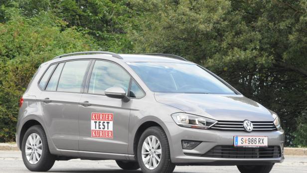 Ein grauer VW Golf steht vor einer grünen Hecke.