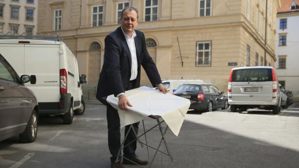 Ein Mann deckt einen kleinen Tisch im Freien mit einem weißen Tuch ab.