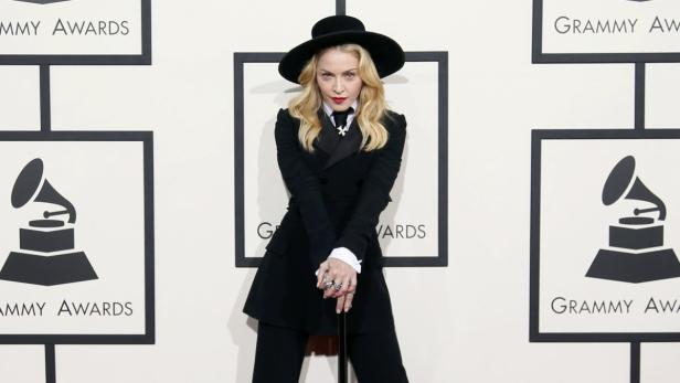 Madonna posiert in einem schwarzen Hosenanzug und Hut vor dem Hintergrund der Grammy Awards.