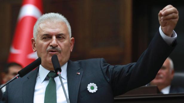 Ein Mann in einem Anzug gestikuliert vor einer türkischen Flagge.