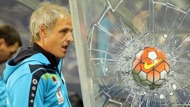 Ein Fußball hat eine Scheibe durchschlagen, während ein Trainer zusieht.