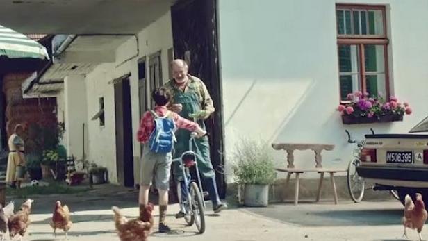Ein Junge mit Fahrrad unterhält sich mit einem älteren Mann vor einem Bauernhaus.