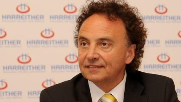 Ein Mann mit lockigem Haar und einem Anzug vor einem Hintergrund mit dem Harreither-Logo.