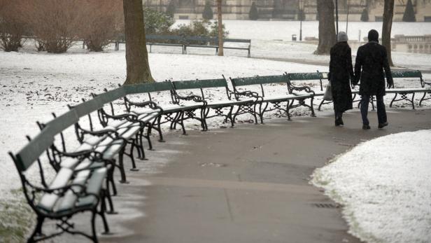 Ein Paar geht im Winter durch einen Park mit schneebedeckten Bänken.