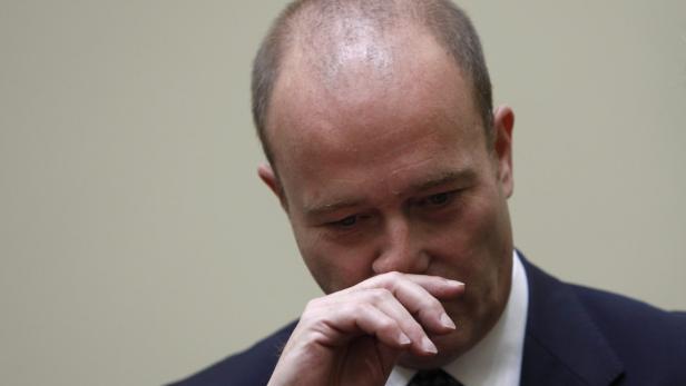 Ein Mann in einem Anzug bedeckt seinen Mund mit der Hand.