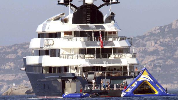 Eine große Yacht mit Wasserspielzeug liegt vor einer felsigen Küste vor Anker.