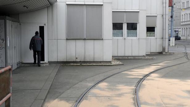 Eine Person betritt ein Gebäude neben einer Straßenbahnschiene.