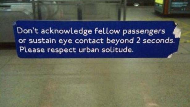 Ein blaues Schild in einer U-Bahn-Station fordert dazu auf, andere Fahrgäste nicht anzuerkennen und keinen Augenkontakt über 2 Sekunden hinaus zu halten.