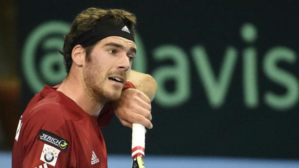 Ein Tennisspieler mit Stirnband lehnt an seinem Schläger.