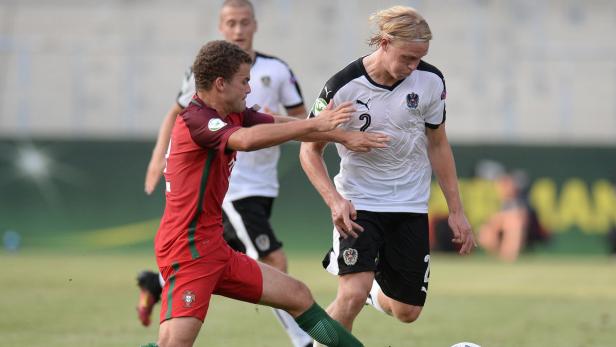 Ein Fußballspieler im roten Trikot versucht, einen Spieler im weißen Trikot zu stoppen.