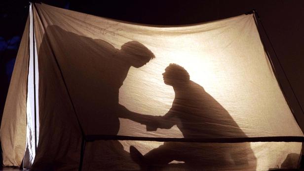 Schattenrisse zweier Personen interagieren hinter einem hell erleuchteten Tuch.