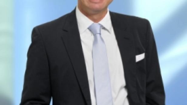 Ein Mann mit Brille, Anzug und Krawatte lächelt in die Kamera.