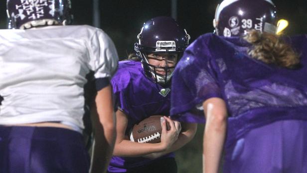 Eine Footballspielerin in lila Uniform hält einen Football in ihren Händen.