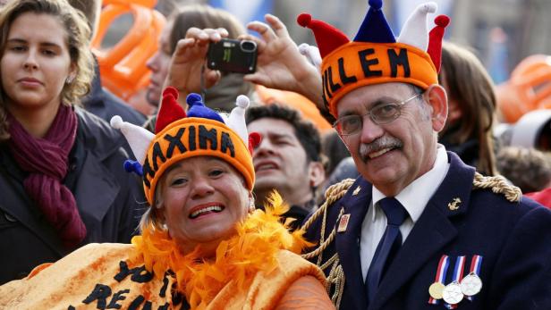 Zwei Menschen mit orangefarbenen Hüten mit der Aufschrift „Willem“ und „Maxima“ lächeln.