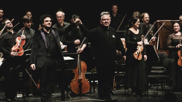 Ein Orchester mit Dirigenten nimmt den Applaus des Publikums entgegen.