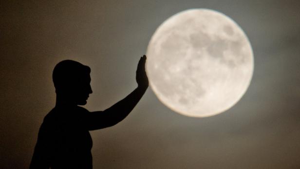 Die Silhouette eines Mannes scheint den Mond zu berühren.