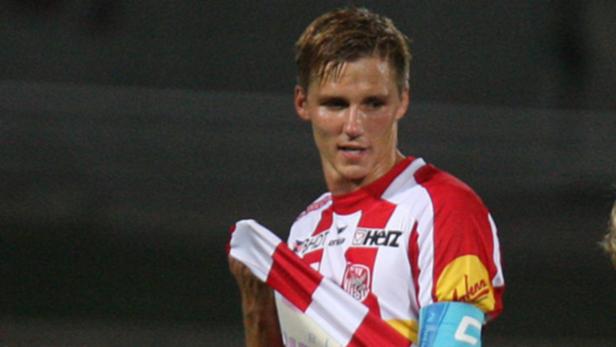 Ein Fußballspieler in einem rot-weiß gestreiften Trikot hält ein Trikot in der Hand.