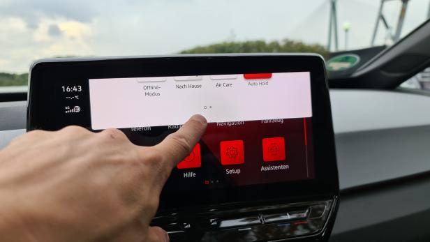 Ein Finger tippt auf den Touchscreen eines Autos, der verschiedene Menüoptionen anzeigt.
