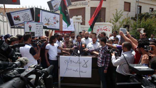 Eine Gruppe von Menschen demonstriert mit libyschen Flaggen und Schildern vor einem Gebäude.