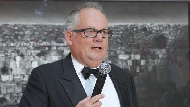 Ein Mann mit Brille und Fliege spricht in ein Mikrofon.