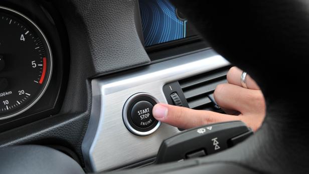 Ein Finger drückt den Startknopf im Innenraum eines Autos.