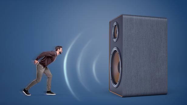 A large vintage speaker emits strong sound-waves and almost sweeps a small aggressive man off his feet.
