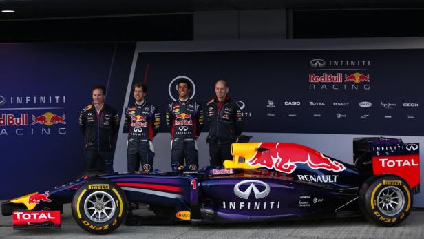 Ein Red Bull Formel-1-Rennwagen mit vier Personen im Hintergrund vor einer Sponsorenwand.