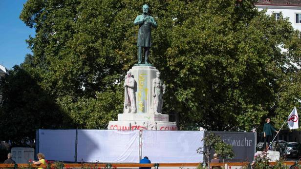 Nachdem das umstrittene Denkmal mit „Schande“-Schriftzügen beschmiert wurde, hat die Stadt es mit einem Bauzaun umhüllt
