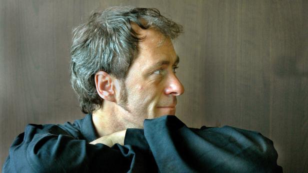 Ein Mann mit grau meliertem Haar und Koteletten blickt zur Seite.