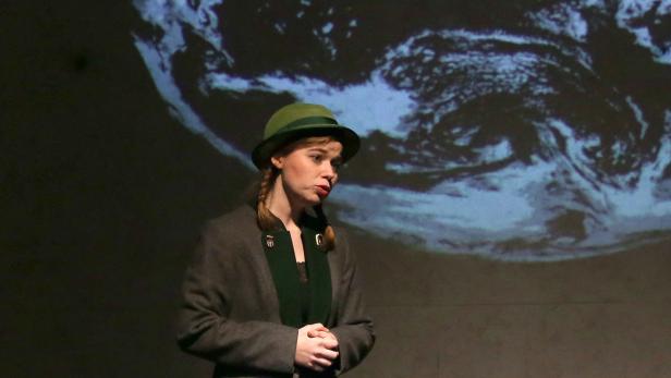 Eine Frau mit Hut steht vor einer Projektion der Erde.