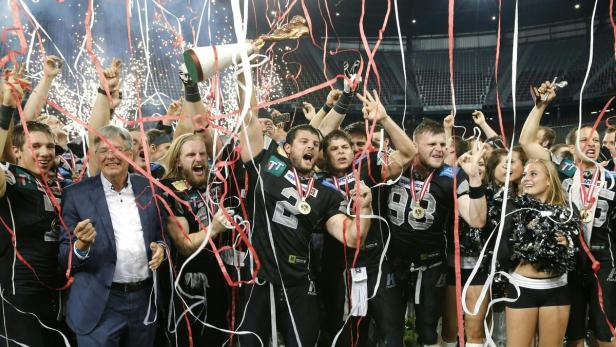Ein American-Football-Team feiert einen Sieg mit Konfetti und einer Trophäe.